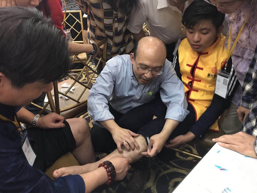 A teacher demonstrating Tung's Acupuncture points to a close group of Acupuncturists